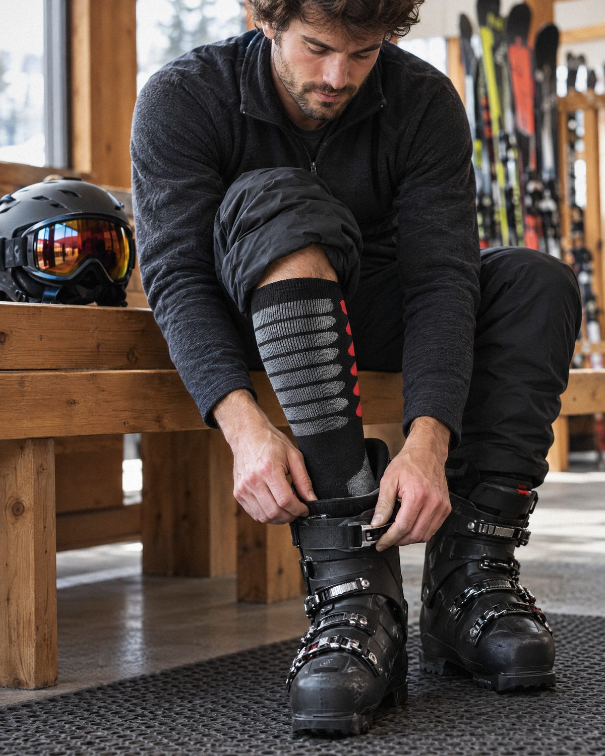 Skier in a lodge buckling his ski boot over Wildler wireless heated socks